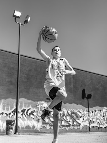 Boy Standing on One Leg Holding Basketball Outdoors
