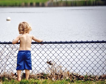 Boy Wearing Blue Shorts Standing over the Purple Metal Rails Overlooking Body of Water
