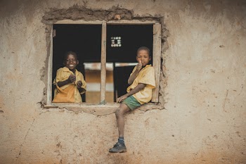 Boys in school uniform sitting on window frame of an unfinished classroom