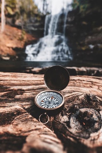 brass-colored compass on brown wooden tree stump in front of waterfalls during daytime