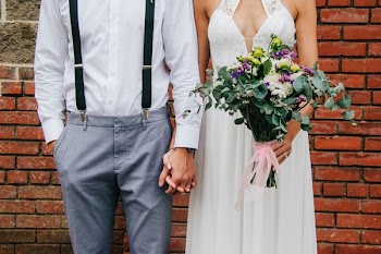 bride and groom holding hands and standing beside brown bricked wall during daytime