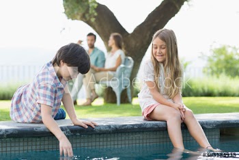 Brother and sister playing at edge of swimming pool