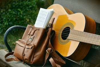 Brown Acoustic Guitar Beside Brown Leather Bucket Backpack on Brown Wooden Bench