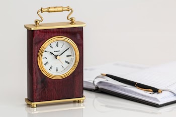 Brown and Brass-colored Desk Clock on White Surface Beside Black Click Pen on Opened Notebook