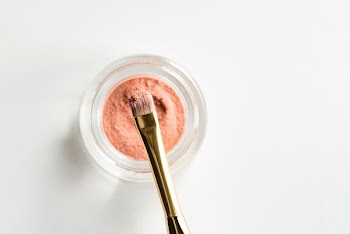 brown makeup brush in front pink powder on glass case