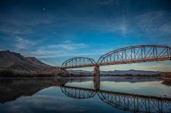 Brown Metal Bridge Reflecting on Clear River Water Beneath Blue Sky