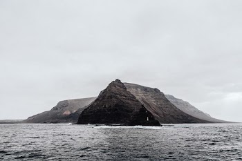 brown mountain beside body of water under grey cloudy sky