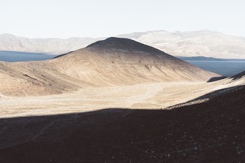 brown mountain near body of water under blue sky at daytime