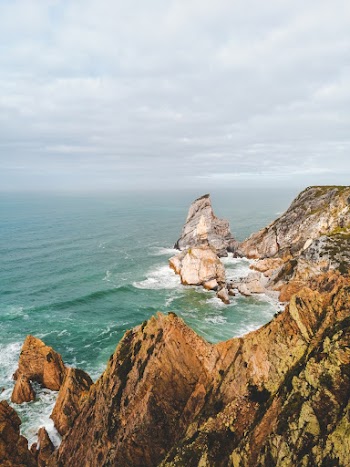 Brown Rock Formation on Sea Under White Clouds