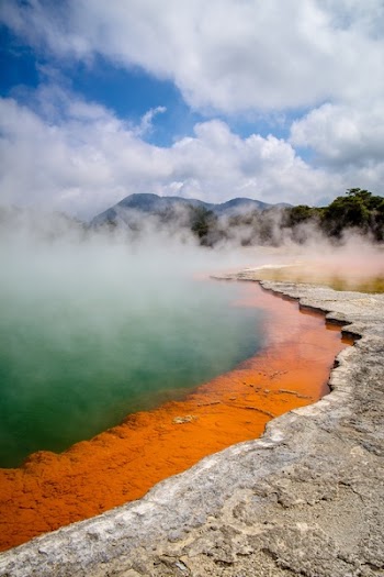 Brown Surface Beside Body of Water in a Distant of Mountains Under White Clouds during Daytime