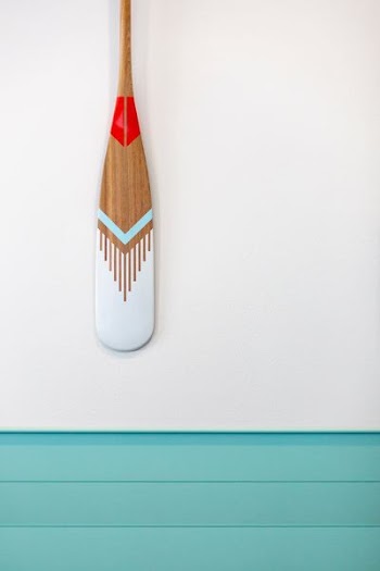 brown, teal, and gray wooden paddle on gray wall