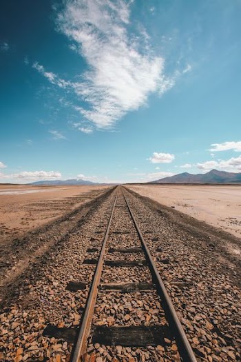 brown train rail in desert under blue and white sky