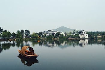 brown wooden boat on body of water overlooking houses by the shore at daytime