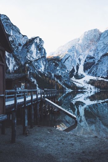 brown wooden bridge near river and snow-capped mountains at daytime
