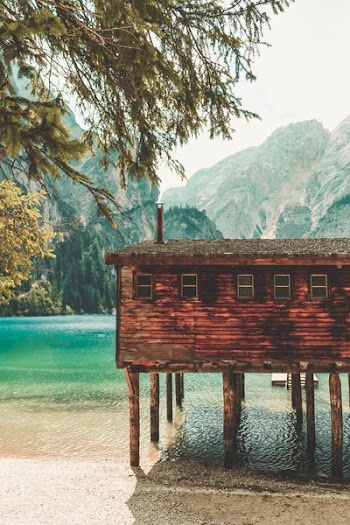 brown wooden house over sea surrounded with mountain