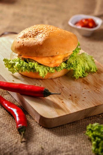 Burger on Top of Wooden Board Near Two Red Chili
