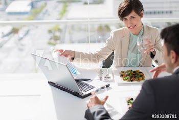 Business people eating lunch and working at laptop in sunny office