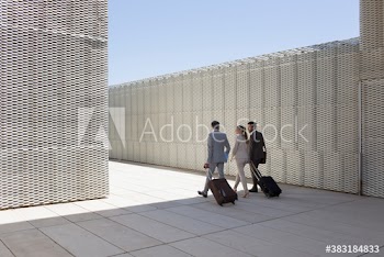 Business people with suitcases walking in modern sunny courtyard