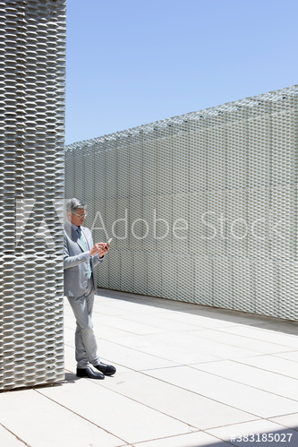 Businessman using smart phone on sunny modern rooftop