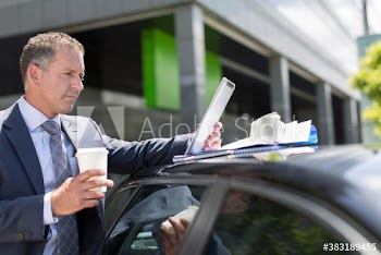 Businessman with coffee using digital tablet at car