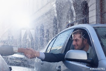 Businessmen shaking hands from cars on rain street