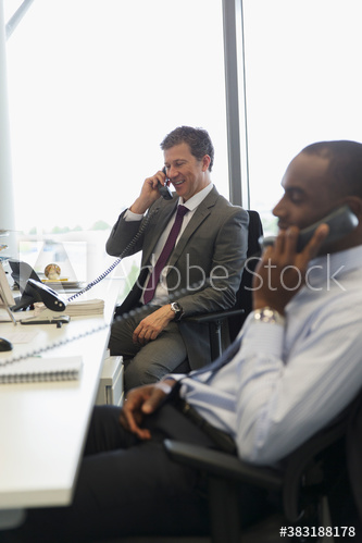 Businessmen talking on telephones in office