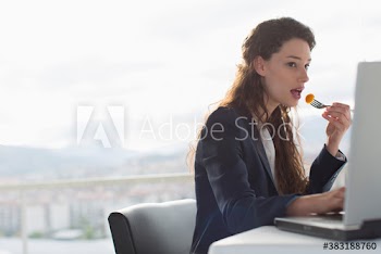 Businesswoman eating lunch and working at laptop in office