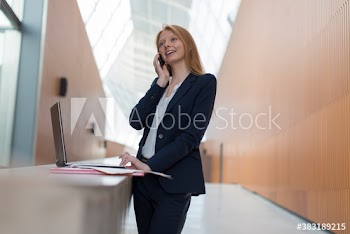 Businesswoman talking on smart phone at laptop in modern office