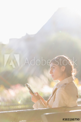 Businesswoman using digital tablet on sunny park bench