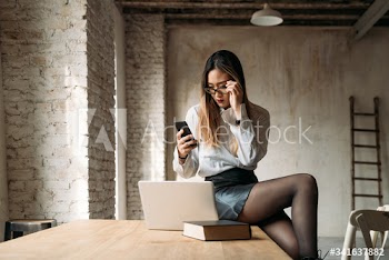 Businesswoman using smartphone and laptop while sitting on table indoors