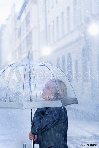 Businesswoman with umbrella talking on smart phone in rain