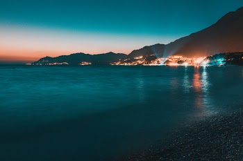 Calm Body of Water Facing Lighted City Near Mountain