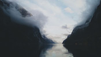 calm body of water near rock formation covered by white smoke at daytime