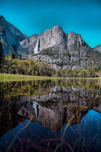 calm body of water overlooking waterfalls and gray rock mountain under blue sky at daytime