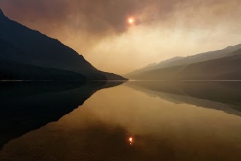 calm body of water under brown clouds and mountains