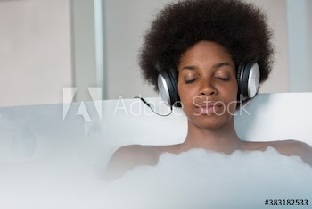 Calm young woman with afro listening to music with headphones in bath