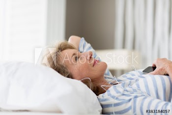 Carefree senior woman relaxing on bed listening to music
