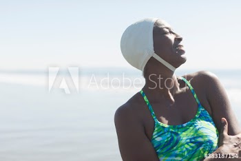 Carefree woman in bathing suit and swimming cap on sunny ocean beach