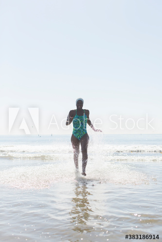 Carefree woman in bathing suit running in sunny ocean surf