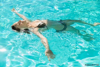 Carefree young woman floating on back in sunny swimming pool