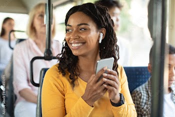Cheerful black lady using smartphone wearing headphones in bus