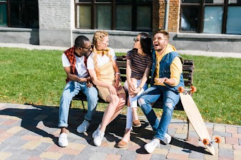 Cheerful multicultural couples resting on bench together on street