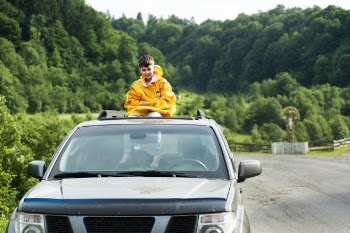 Child in Yellow Jacket Sitting on Roof of Nissan Frontier Through the Sunroof