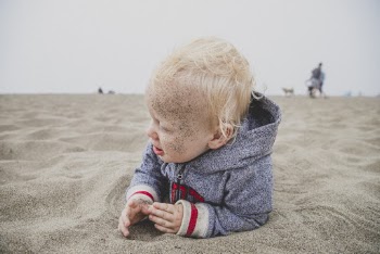 Child Lying on Sand With Sand over His Face