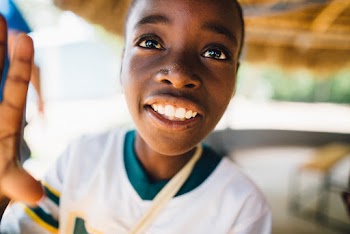 Child Wearing White and Green V-neck T-shirt Grinning