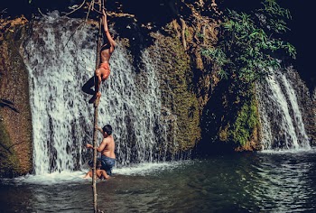 Children Climbing On Tree Branch Near Waterfalls