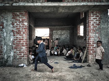 Children Sitting on Floor Inside Building and Another Two Children Walking
