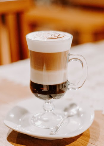 Clear Footed Drinking Glass Filled With Cappuccino on White Ceramic Saucer and Table