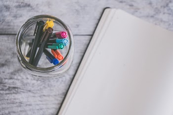 Clear Glass Jar Filled of Coloring Pens Beside of White Sketch Pad