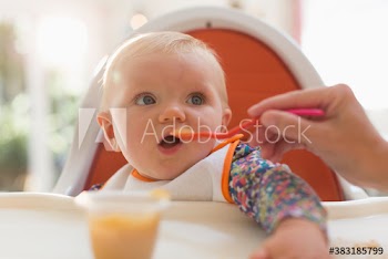 Close up baby girl being fed in high chair